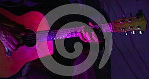 Close up man hands playing guitar on stage live in concert with neon lights photo