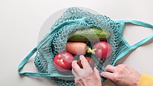 Close up of man hands puts vegetables into eco string bag at supermarket