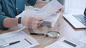 Close-up of man hands reviewing financial documents with magnifying glass. Business work process in bookkeeping office