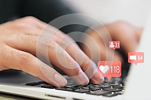 Close up of man hands using laptop on desk with creative social media icons hologram on blurry background. Community, likes,