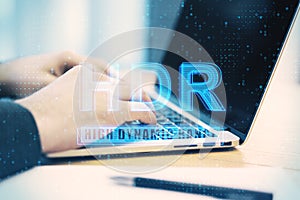 Close up of man hands using laptop on desktop with abstract golowing HDR hologram, Blurry background. Technology and display