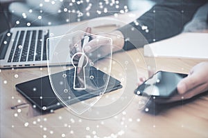 Close up of man hands using laptop, tablet and smartphone at desktop with abstract padlock shield inside polygonal sphere on