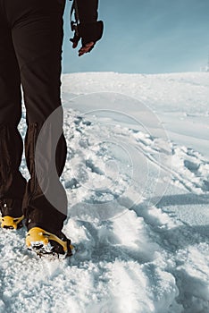 Close up of a man hiking on a mountain covered on snow, in boots with shoe spikes. Outdoor winter trekking