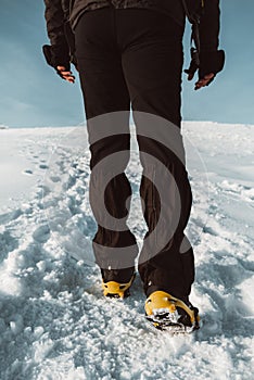 Close up of a man hiking on a mountain covered on snow, in boots with shoe spikes. Outdoor winter trekking