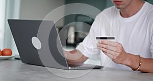 Close-up man holding credit card in his hands and paying for purchases on Internet using a laptop while sitting at home