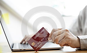 Close-up of a man holding a credit card and operating a laptop.