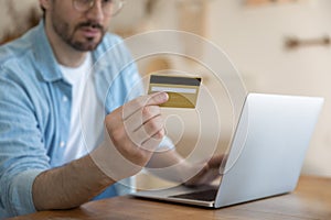 Close up man holding credit card, using laptop, paying online