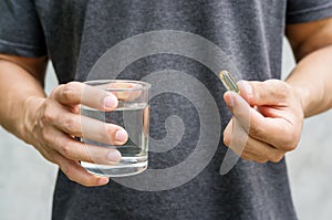 Close up of a man holding a fish oil capsule and a glass of water