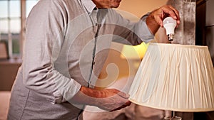 Close Up Of Man At Home Changing Bulb In Lamp To Energy Saving LED Unit