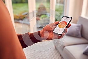 Close Up Of Man At Home Looking At App On Smart Phone To Control Heating