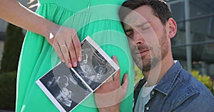 Close-up of a man hugging his pregnant wife and stroking her belly, side ultrasound photo of the baby