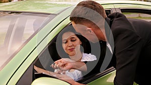 Close-up of a man in a jacket giving a young woman the keys to a new car.