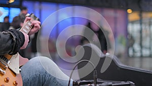 Close-up of a man in jeans playing a rock guitar in a crowded city.