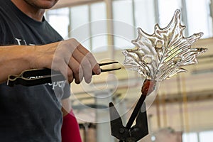Close up man makes a leaf from the glass for vase or chandelier using tongs and blowpipe photo
