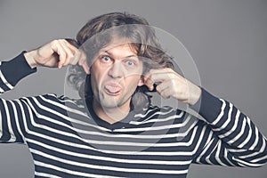 Close up of man making silly monkey face isolated on grey background. Guy grimaces monkey. Funny male holding his ears