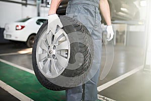 Close up of man mechanic carrying a tire in tire service