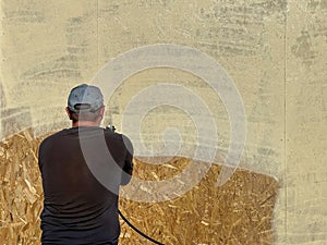 Close-up a man paints his house beige with a spray gun. worker spraying paint over timber wood. Construction worker with spray gun