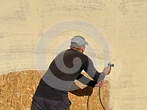 Close-up a man paints his house beige with a spray gun. worker spraying paint over timber wood. Construction worker with spray gun
