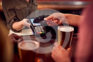Close Up Of Man Paying For Drinks At Bar Using Contactless Card