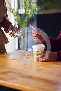 Close Up Of Man Paying Female Server In Coffee Shop Using Debit Or Credit Card