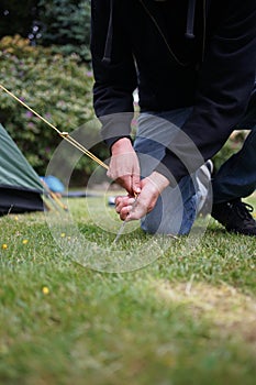 Close up of a man pegging down a tent on grass.