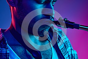 Close-up of man playing saxophone, jazz melodies against gradient pink-blue background vibrant lighting.