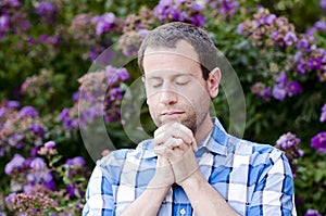 Close up of man praying alone in front of purple flowers.