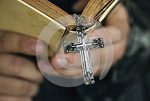 Close up of a man reading a bible with cross hanging religion and belief concept