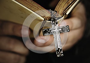 Close up of a man reading a bible with cross hanging religion and belief concept