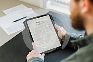 Close up man reading limited warranty tamplate on tablet.