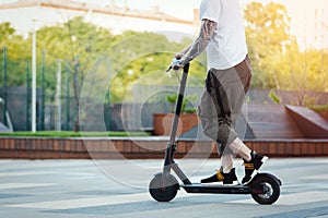 Close up of man riding black electric kick scooter at beautiful park landscape