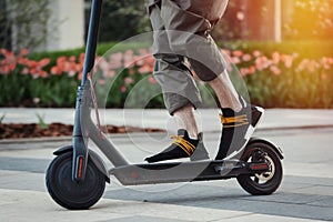 Close up of man riding black electric kick scooter at beautiful park landscape