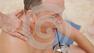 Close-up of a man rubbing sunscreen into the shoulders and back of a fat friend on the beach.