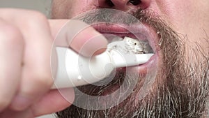 Close up of man`s bearded face who brushes his teeth with tooth brush and toohpaste.
