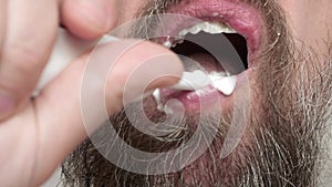 Close up of man`s bearded face who brushes his teeth with tooth brush and toohpaste.