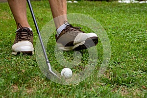 Close-up of man`s feet with golf shoes and out of focus golf club and ball, on grass, horizontal,