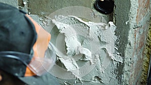 Close-up of a man's gloved hand applying plaster to a concrete wall with a trowel. The concept of finishing the rooms.