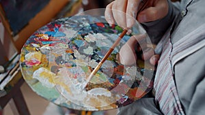 Close-up of man`s hand artist mixing colors on palette then painting picture