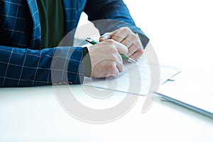 Close-up of man`s hand in business suit, holding pen on background of papers, sitting at table in office. Businessman. Business