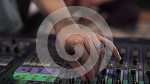 Close-up of a man's hand controls the sound, a professional mixing console in the studio, with LED backlight