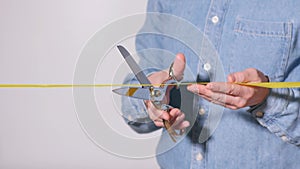 Close Up of a man's hand cutting a yellow ribbon with shiny scissors