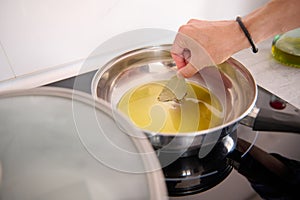 Close-up of a man& x27;s hand holding a bay leaf and seasoning the olive oil frying in a pan while cooking dinner at home