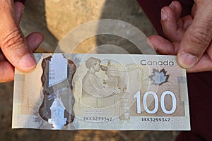A close up of a man`s hand holding Canadian money- $100 bill
