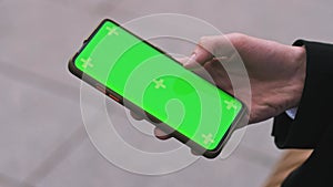 Close-up of a Man's Hand Holding Green Mock-up Screen Smartphone. Modern Mobile Phone. In the Background outdoors