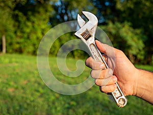 Close-up of a man`s hand holding an old adjustable wrench. Blurry green background. The concept of a tool for work. Copy space