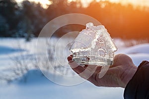 Close-up of man's hand holding small glass, crystal house against background of winter landscape.