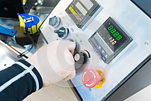 A close-up of a man`s hand holds a rotary switch on the equipment control panel with instruments.