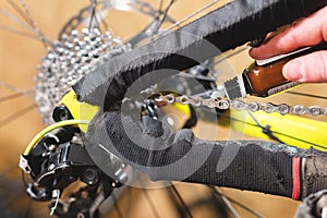 Close-up of a man`s hand, led by masters, lubricate the bicycle chain of a mountain bike with a special lubricant in the