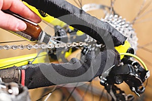 Close-up of a man`s hand, led by masters, lubricate the bicycle chain of a mountain bike with a special lubricant in the