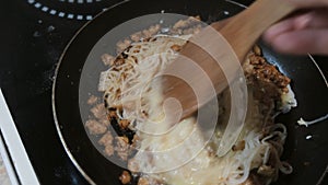 Close-up of a man`s hand mixes with a wooden spatula spaghetti, minced meat and egg in a pan